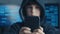 Young hooded boy using a smartphone device at data center. Portrait of Genius boy wonder hacks system at cyberspace.