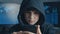 Young hooded boy using a smartphone device. Portrait of Genius boy wonder hacks system at cyberspace.