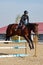 Young horsewoman on brown horse overcomes an obstacle outdoors, copy space. Equestrian sport.