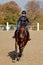 Young horsewoman riding on brown horse in paddok outdoors, copy space.