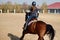 Young horsewoman riding on brown horse in paddok outdoors, copy space.