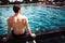 Young hot man resting at swimpool. Back view of guy sitting at water alon and look forward. Enjoy his time lonely in