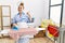 Young housekeeper woman ironing clothes at home smiling happy and positive, thumb up doing excellent and approval sign