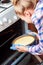 Young housewife taking cheesecake out of oven in kitchen