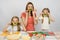 Young housewife with two daughters having fun holding sprig of parsley as a mustache at kitchen table when sharing cooking