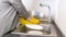 Young housewife in yellow rubber gloves washing plates in kitchen sink