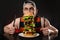 Young hungry man with cutlery eating huge burger on black