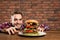 Young hungry man eating huge burger at table.