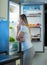 Young hungry woman looking at open refrigerator and choosing something to eat