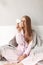 Young ill lady in sleepwear sitting with plaid on bed and thoughtfully looking on pills at home