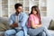 Young Indian couple on couch, appearing distant and pensive