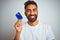 Young indian customer man holding credit card standing over isolated white background with a happy face standing and smiling with