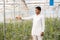 Young indian farmer touch plant standing at his poly house or greenhouse, agriculture business and rural prosperity concept. man