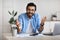 Young indian freelancer guy sitting at desk in office, talking at camera