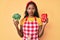 Young indian girl wearing apron holding broccoli and red pepper skeptic and nervous, frowning upset because of problem
