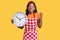 Young indian girl wearing cook apron holding big clock annoyed and frustrated shouting with anger, yelling crazy with anger and