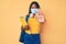 Young indian girl wearing medical mask holding student backpack and books with open hand doing stop sign with serious and