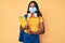 Young indian girl wearing medical mask holding student backpack and books thinking attitude and sober expression looking self