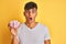 Young indian man holding bowl with marshmallows over isolated yellow background scared in shock with a surprise face, afraid and