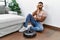 Young indian man sitting at home by vacuum robot thinking looking tired and bored with depression problems with crossed arms