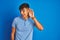 Young indian man wearing casual polo standing over isolated blue background smiling with hand over ear listening an hearing to