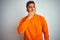 Young indian man wearing orange sweater over isolated white background bored yawning tired covering mouth with hand