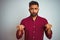 Young indian man wearing red elegant shirt standing over isolated grey background Pointing down looking sad and upset, indicating