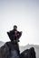 Young indian mountaineer sitting on the top of the mountain on a cliff with a backpack and a stick, enjoying the view from the top