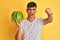 Young indian shopkeeper man holding watermelon standing over isolated yellow background annoyed and frustrated shouting with