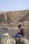 Young indian traveler with long hair sitting near a lake with some books. travel and freedom concept