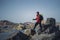 Young indian traveler standing confidently on top of the mountain over a cliff, wearing a red snow jacket. Confident and success