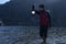 Young indian traveler standing near a lake in the mountains with a lantern, getting ready for camping in the night