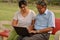 Young Indian woman manager in western formals / shirt helping old Indian man on a laptop promoting digital literacy for elderly in