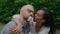 A young international couple in love sitting on the grass, the man holding a flower in his teeth and looking directly