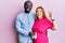 Young interracial couple expecting a baby holding shoes doing ok sign with fingers, smiling friendly gesturing excellent symbol