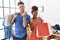 Young interracial couple holding shopping bags at retail shop doing money gesture with hands, asking for salary payment,