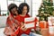 Young interracial couple smiling happy unboxing christmas gift sitting on the sofa at home