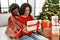 Young interracial couple smiling happy unboxing christmas gift sitting on the sofa at home