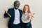 Young interracial couple wearing business and elegant clothes smiling friendly offering handshake as greeting and welcoming