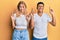 Young interracial couple wearing casual white tshirt gesturing finger crossed smiling with hope and eyes closed