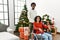 Young interracial couple with woman sitting on wheelchair by christmas tree with a happy and cool smile on face