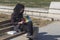 A young Iranian girl in modern clothes and a black shawl on her head reads a book on a bench in Imam Square