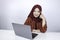 Young Islam woman is smiling face with thinking gesture looking on the blank space in the front of laptop