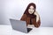 Young Islam woman is smiling face with thinking gesture looking on the blank space in the front of laptop