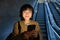 Young Japanese girl standing with smartphone, going down escalator with mobile phone, commuting in city, using public