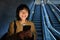 Young Japanese girl standing with smartphone, going down escalator with mobile phone, commuting in city, using public