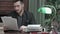 Young journalist reading printed articles sitting at the desk with typewriter