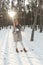 A young and joyful Caucasian girl in a brown coat holds a snowball in a snow-covered forest in winter. Fisheye Photo