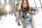 A young and joyful Caucasian girl in a brown coat sculpts a snowball in a snow-covered forest in winter