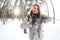 A young and joyful Caucasian girl in a brown coat sculpts a snowball in a snow-covered forest in winter